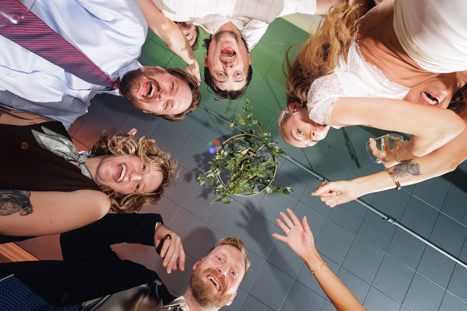 Group of friends laughing and posing in a circle viewed from below, holding flowers at a celebration.
