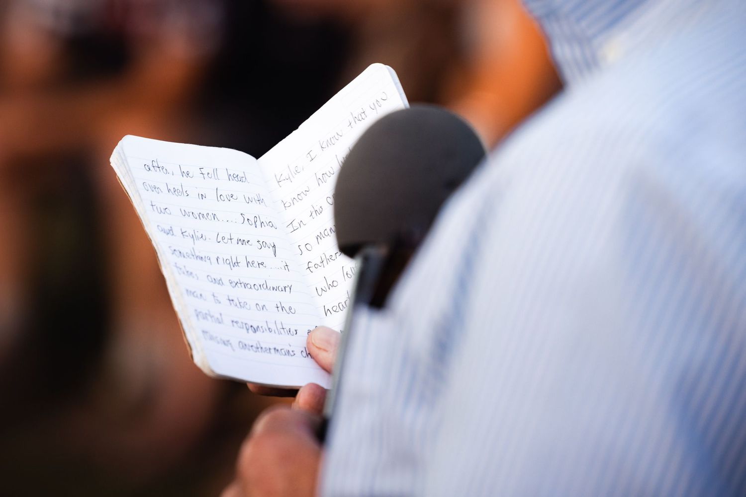 Someone reads from handwritten notes while holding a microphone during a speech or presentation.