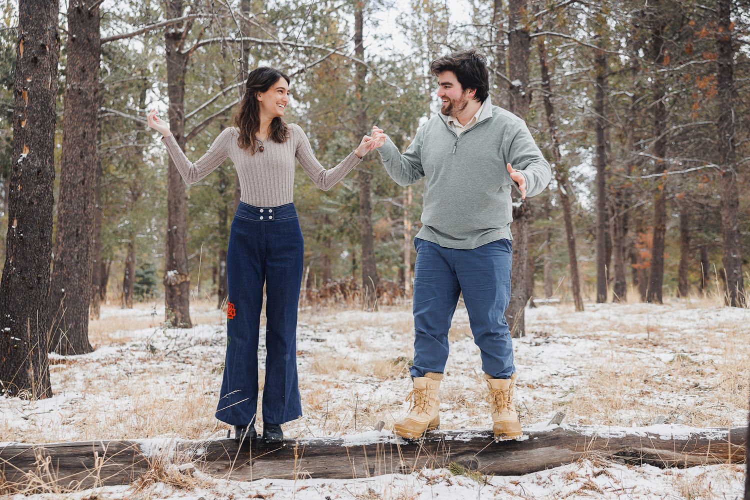 A couple shares a joyful moment together in a snowy forest setting during winter.
