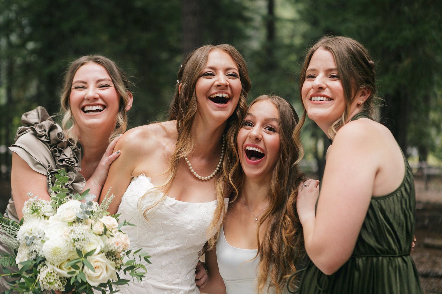 Joyful wedding party members share laughter and embraces while posing in a forest setting.