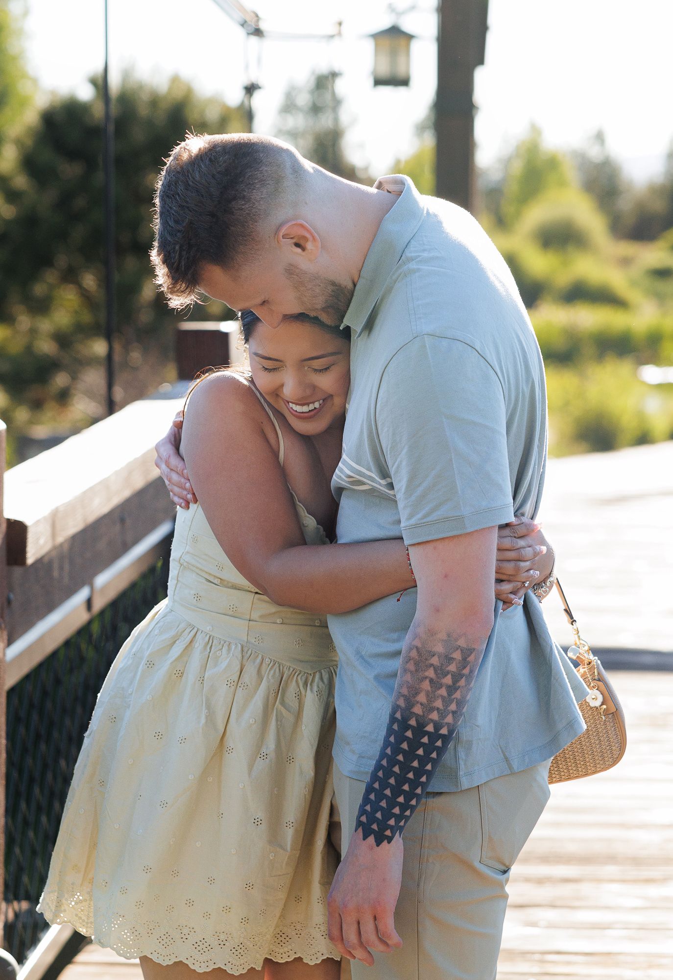 A smiling couple shares a warm hug on a wooden deck outdoors on a sunny day.