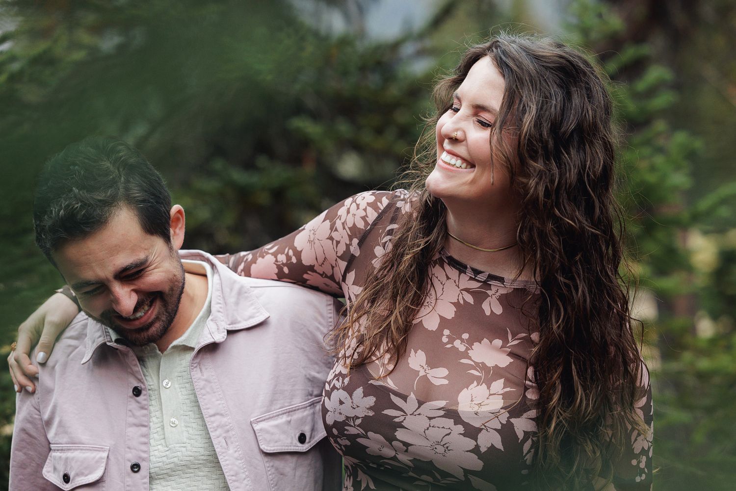 A couple shares a joyful candid moment together outdoors, with natural greenery in the background.