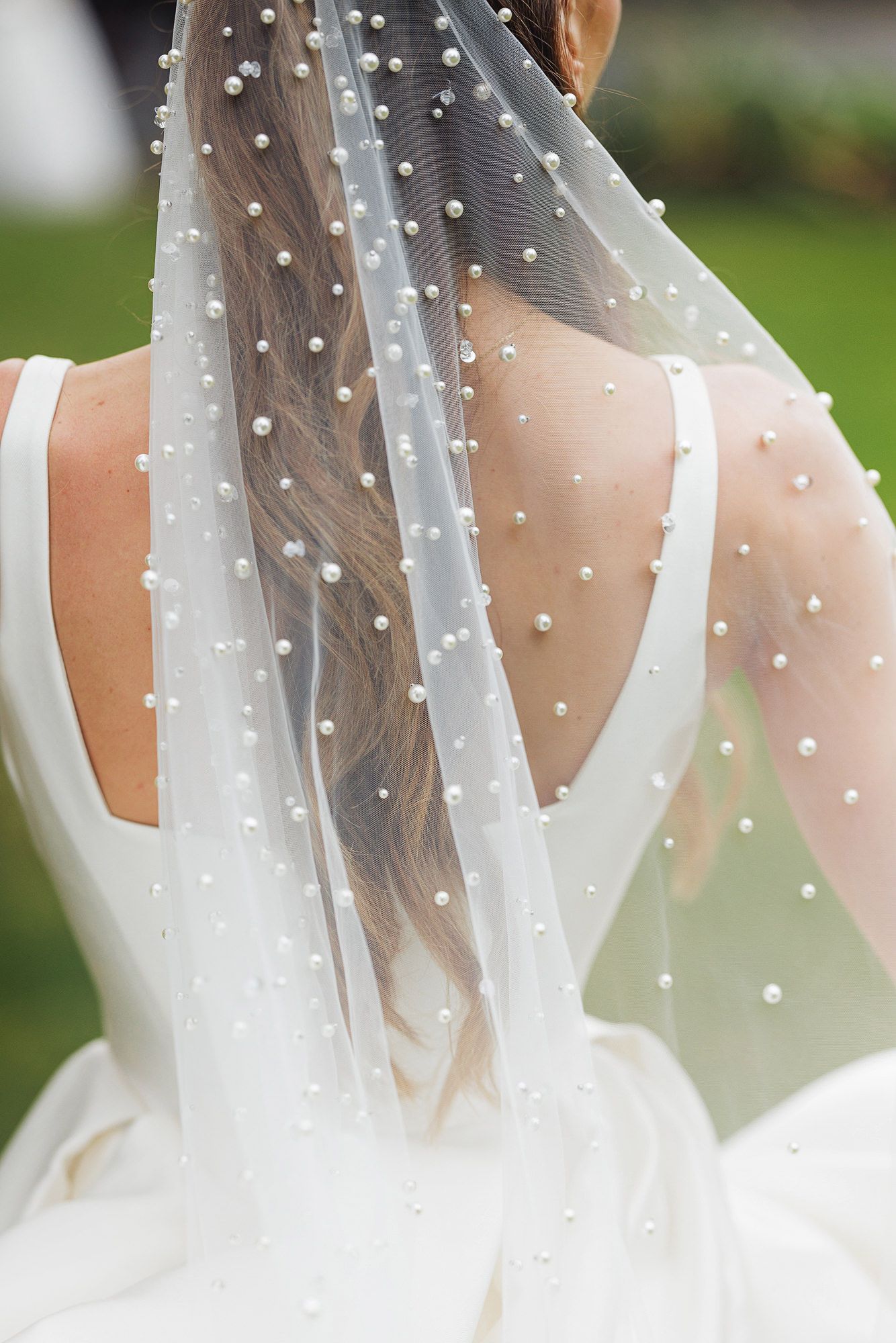 Bride wearing a pearl-embellished wedding veil over a braided hairstyle with a low-back white gown.