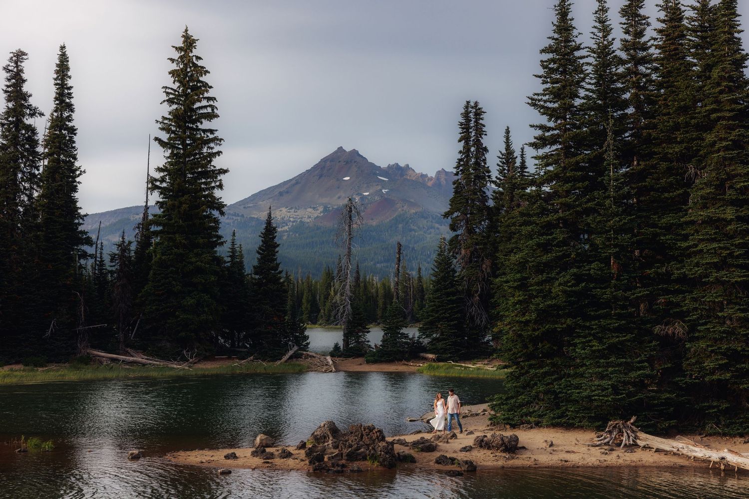 A scenic mountain lake surrounded by evergreen trees and snow-capped peaks reflecting in calm waters at sunset.