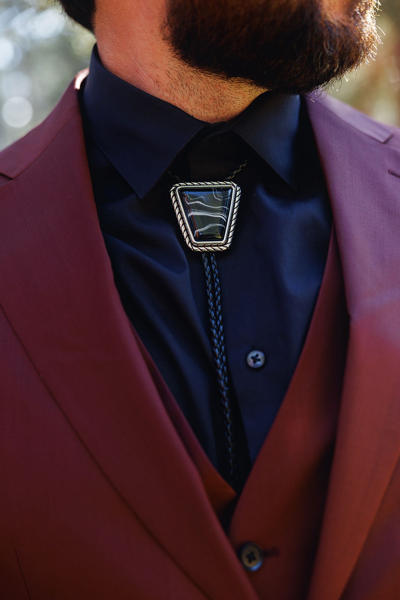 A close-up detail of formal attire showing a navy blue shirt with a dark bolo tie against a burgundy suit jacket.