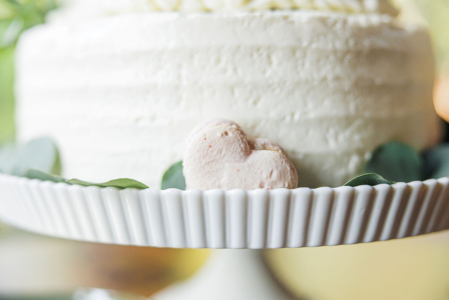 Close-up view of a simple white wedding cake with textured buttercream frosting and fresh green botanical decorations.