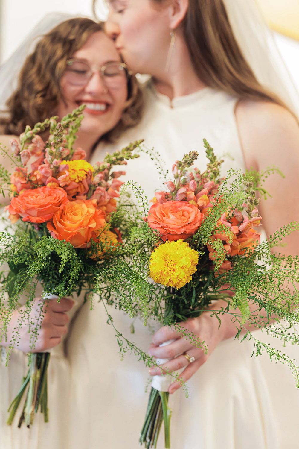 Three colorful wedding bouquets with orange and yellow flowers paired with delicate greenery against a white background.