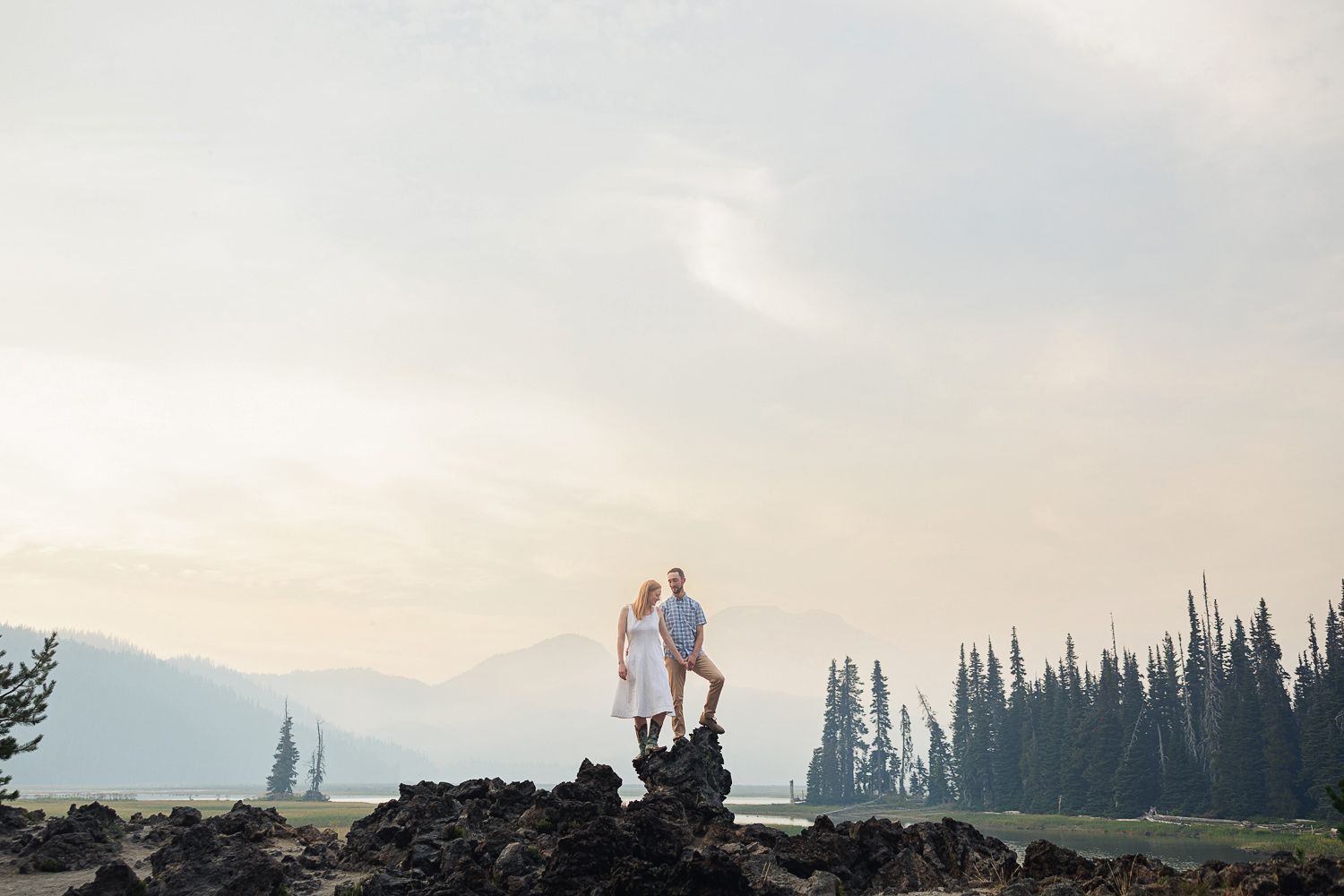 A scenic view of someone walking on a mountain ridge during sunset with silhouetted evergreen trees in the distance.