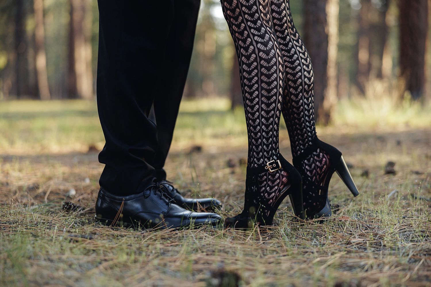 Close-up of a couple standing outdoors, man in black dress shoes and woman in patterned tights and black high heels.