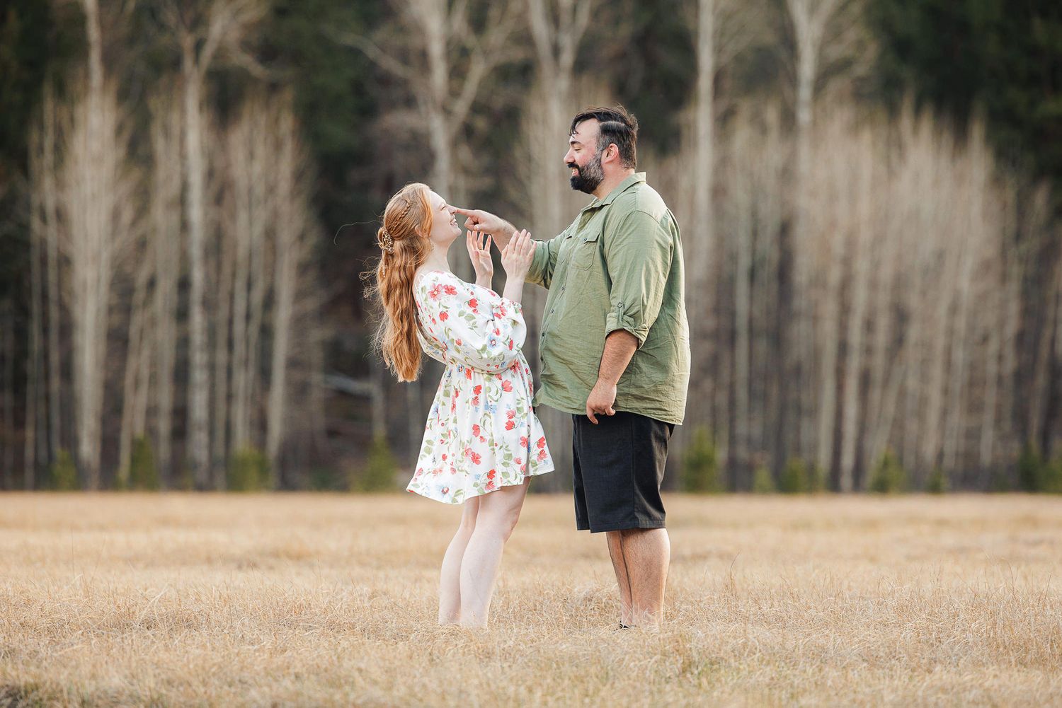 Couple dancing barefoot in a golden field with trees in background, woman in floral dress, man in green shirt.
