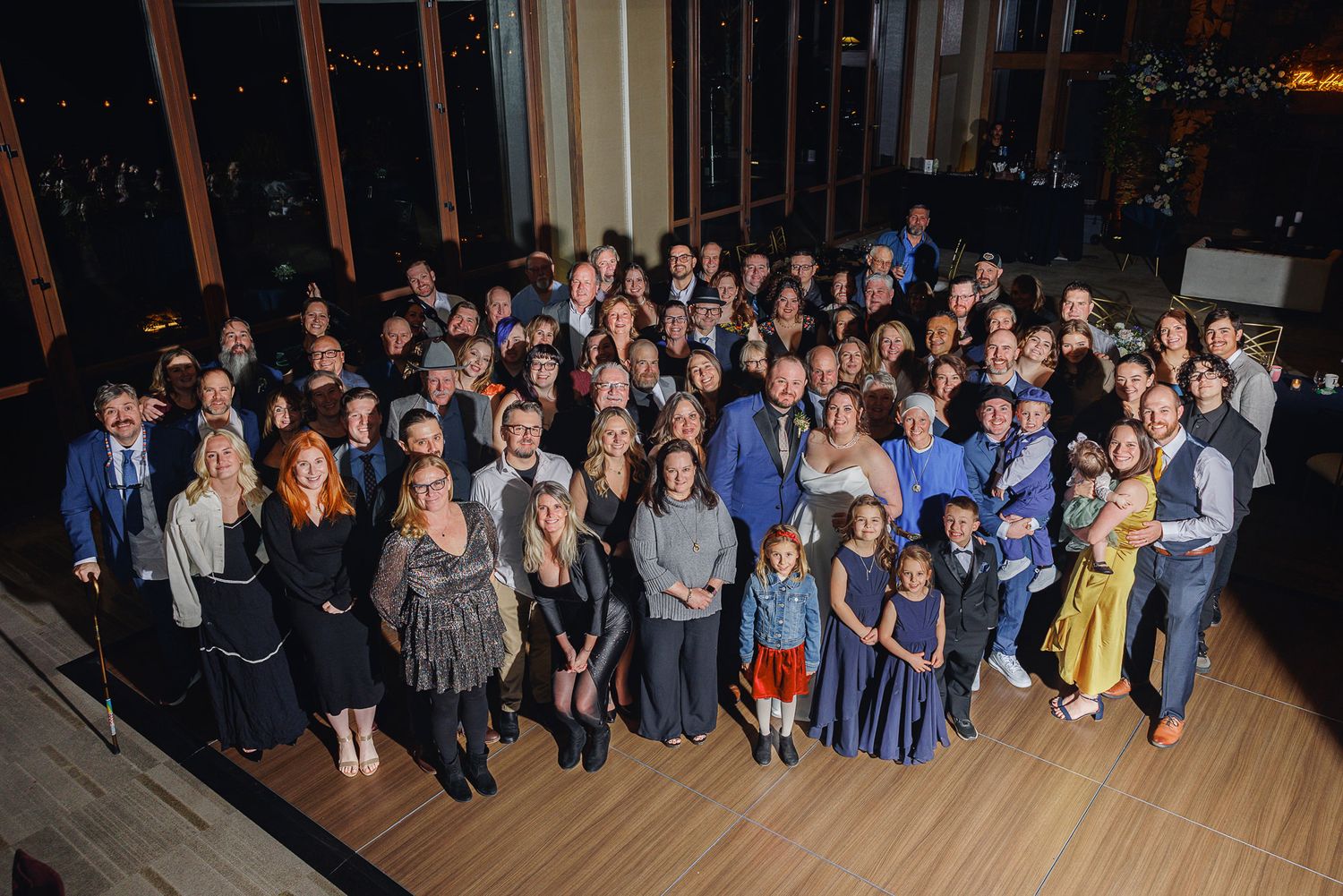 Large group of wedding guests gathered on a dance floor at an evening reception celebration.