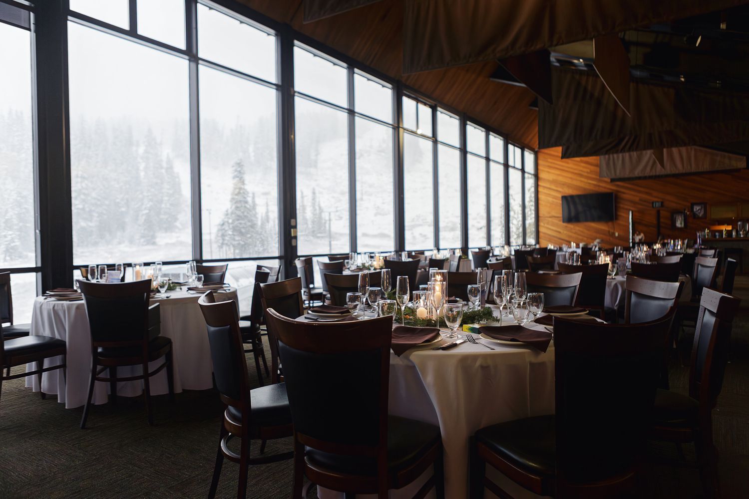 Elegant restaurant dining room with panoramic windows offering scenic views and white-clothed tables set for service.
