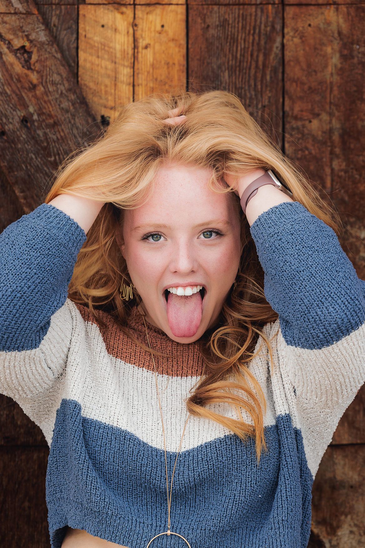 Playful winter portrait against wooden wall wearing blue and white sweater with silly expression.