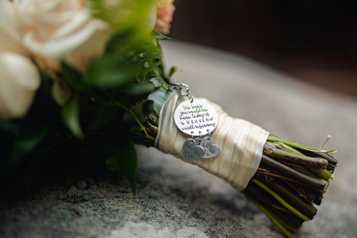 A wedding bouquet wrapped in white ribbon with a decorative silver charm or pendant attached.