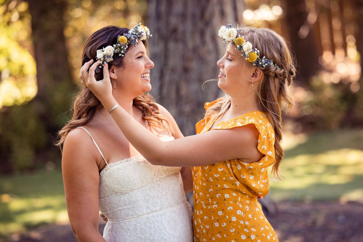 Two people wearing floral crowns embrace outdoors in golden sunlight.