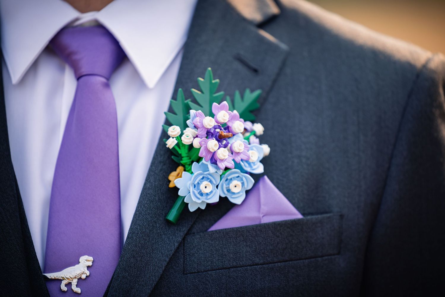 Close-up of a grey suit jacket with purple tie and delicate purple and blue floral boutonniere.