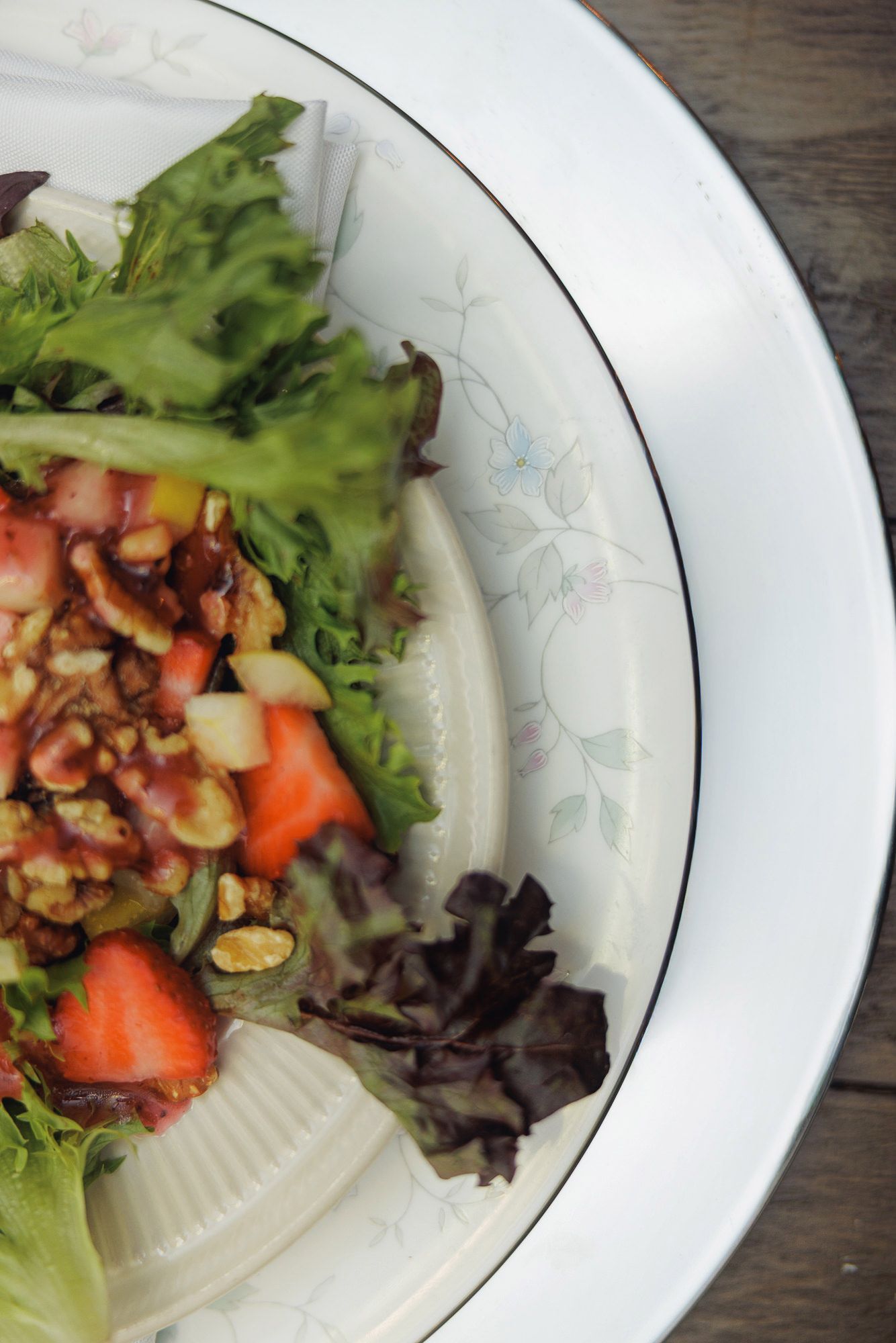 Fresh garden salad with strawberries, walnuts, and mixed greens served on a white floral china plate.