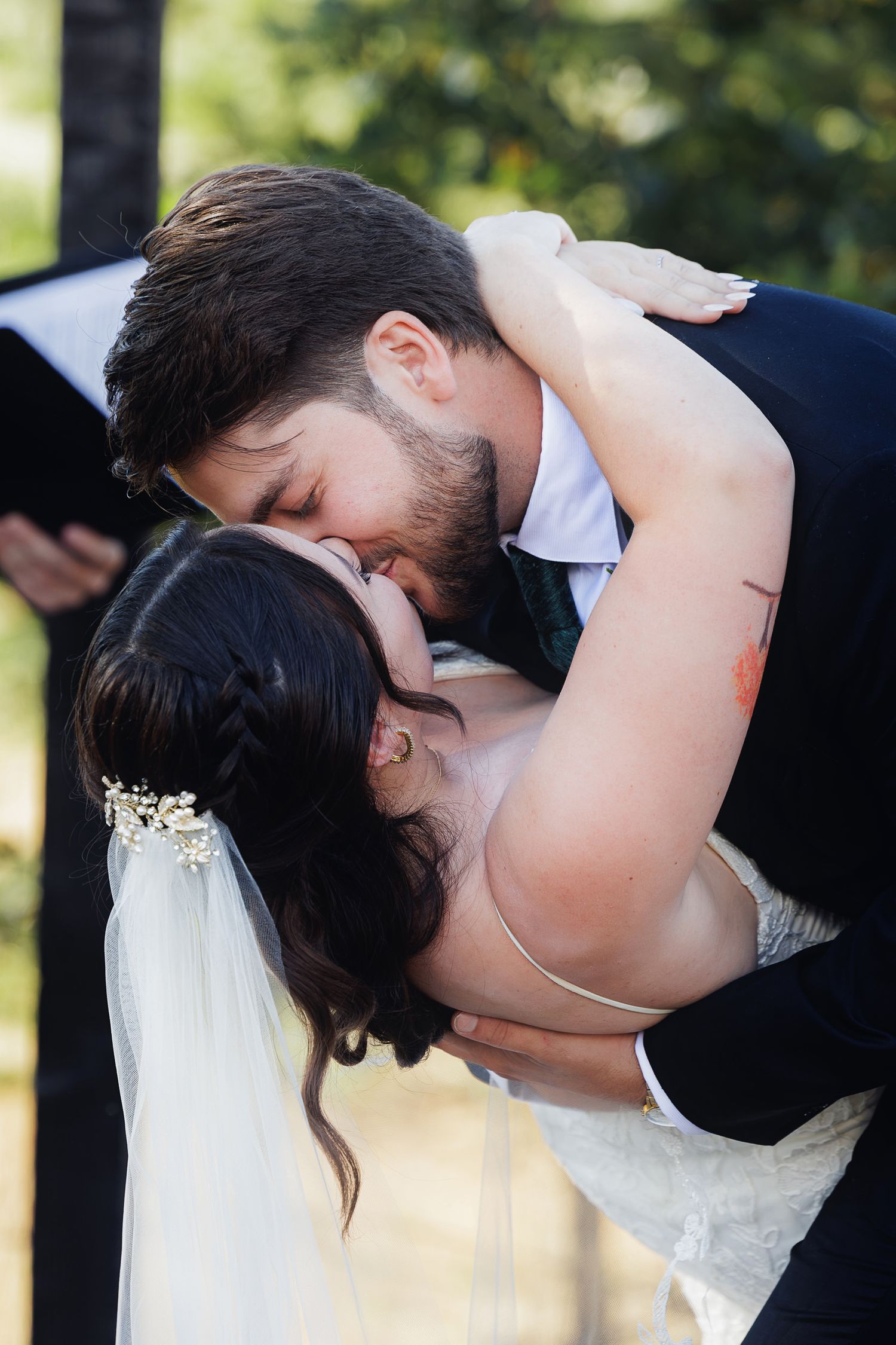 A bride and groom share their first kiss during an outdoor wedding ceremony, with the groom dipping the bride romantically.