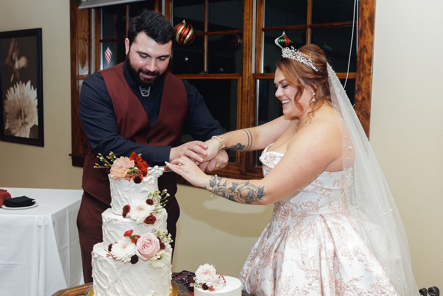 A couple cuts into their elegant three-tiered wedding cake decorated with burgundy and white flowers.