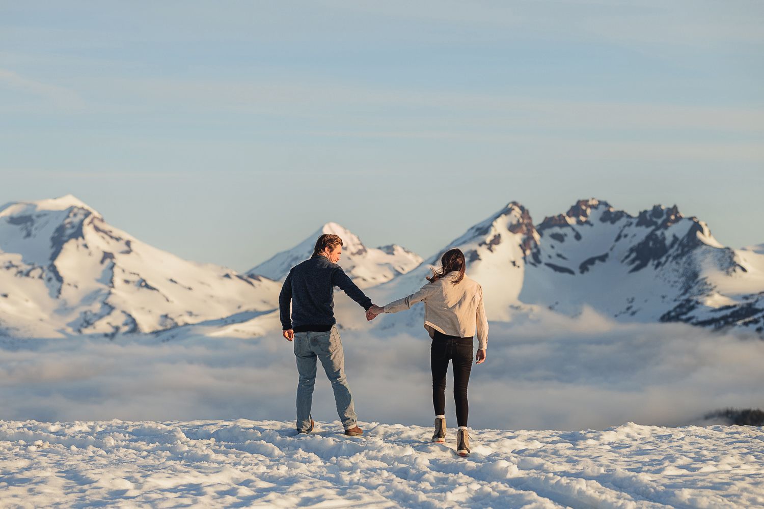 Couple enjoys a playful moment in the snow with majestic mountain peaks in the background.