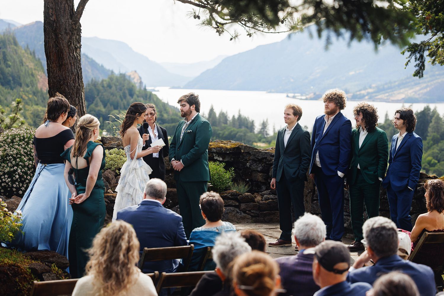 Outdoor wedding ceremony on a scenic overlook with mountain lake views, wedding party in teal and navy attire.