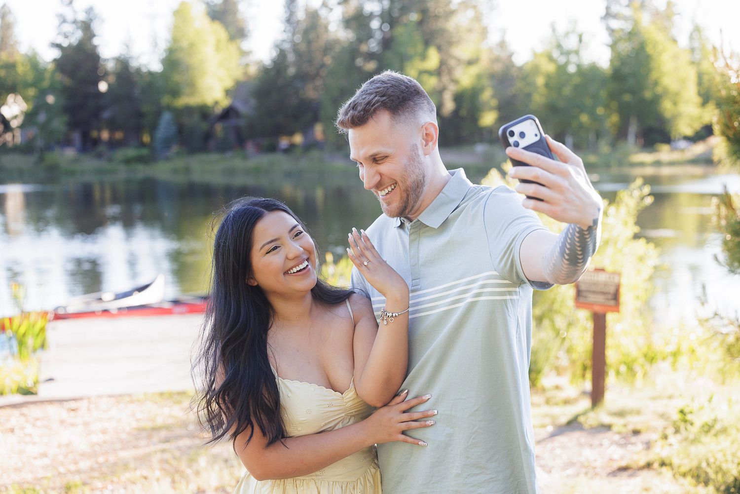 Happy couple taking a selfie by a scenic lake on a sunny day outdoors.