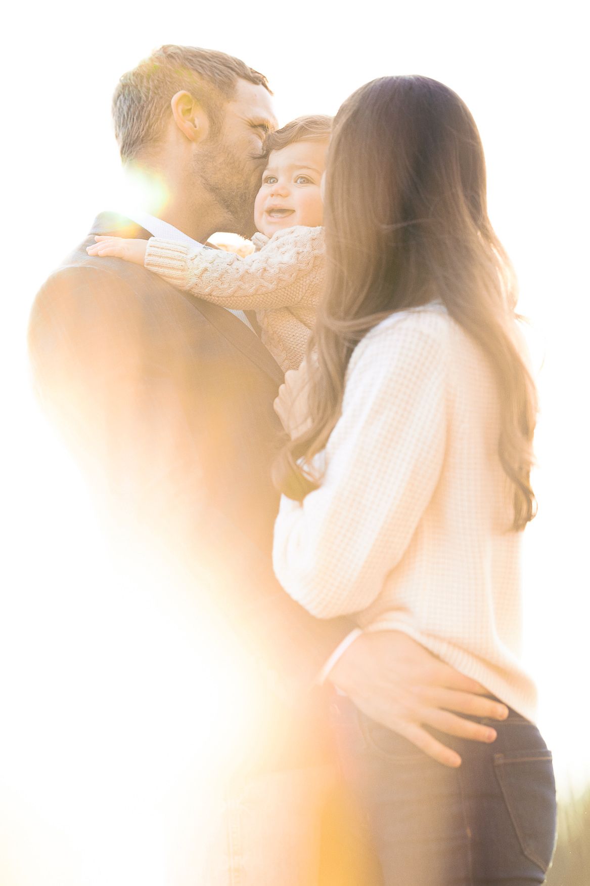 Backlit family embrace captured in soft golden sunlight.