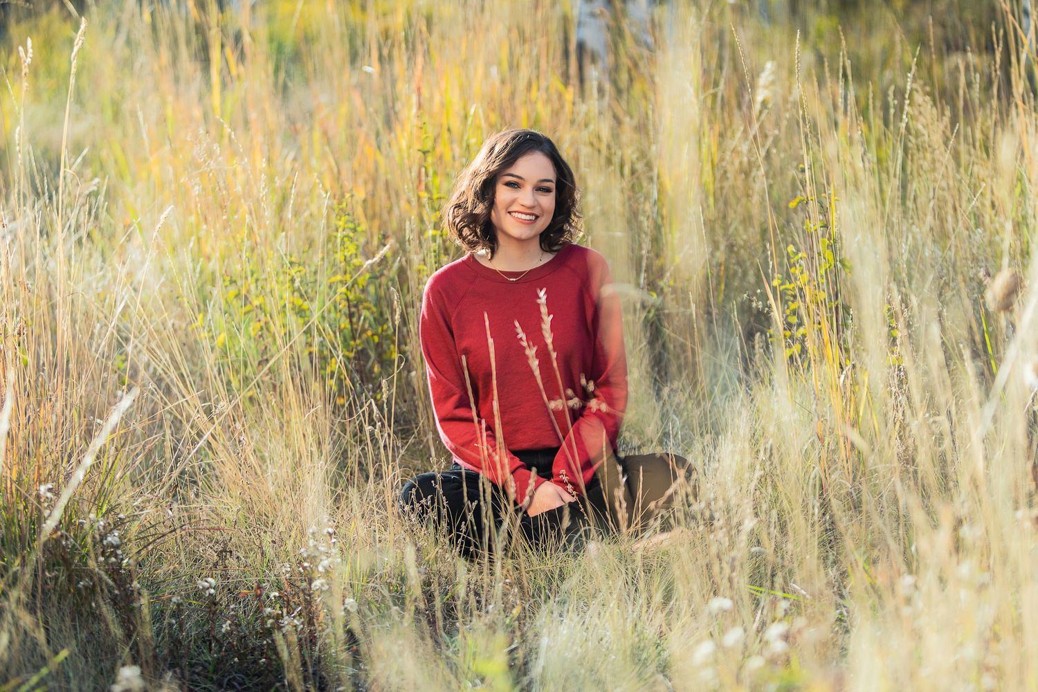 Person in red sweater sitting among tall golden grasses.