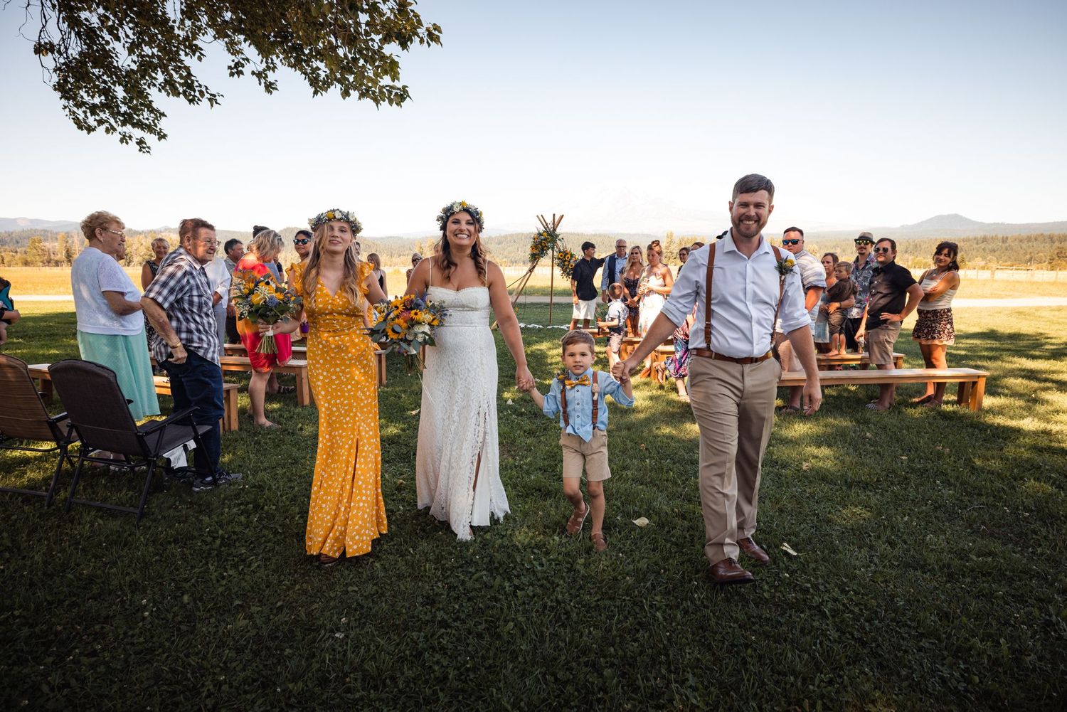Wedding guests celebrate outdoors on a grassy field at sunset during a casual countryside celebration.