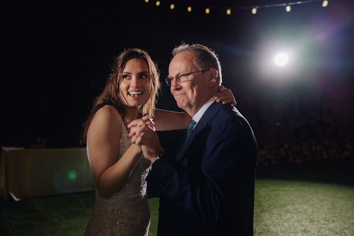 A couple dances together under nighttime lighting at an outdoor reception.