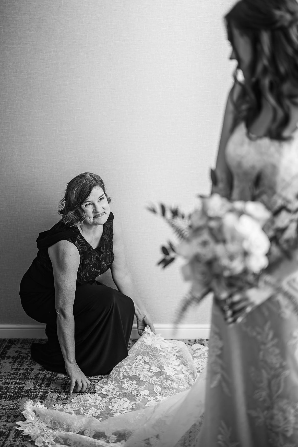 Black and white photo of wedding dress preparation with helper adjusting details.
