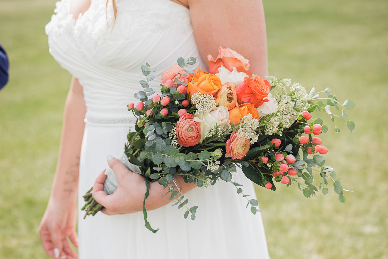 Bride in white dress holding a lush wedding bouquet with orange ranunculus, coral berries, and eucalyptus greenery.