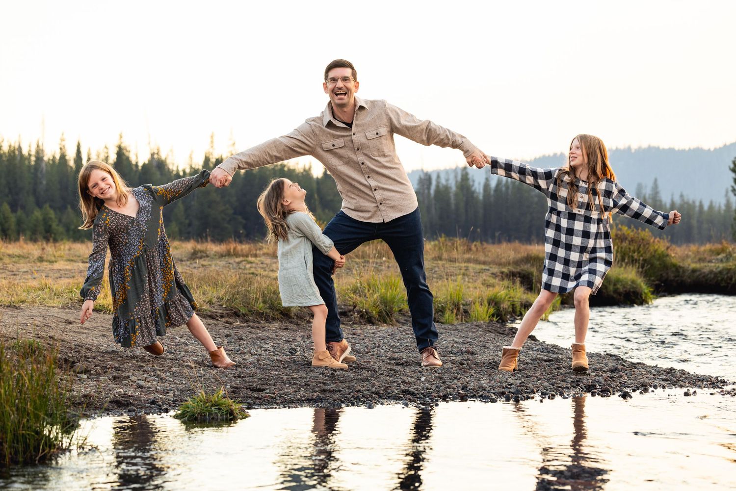 Joyful family playing and balancing together on rocks by a mountain stream in plaid and casual clothing.