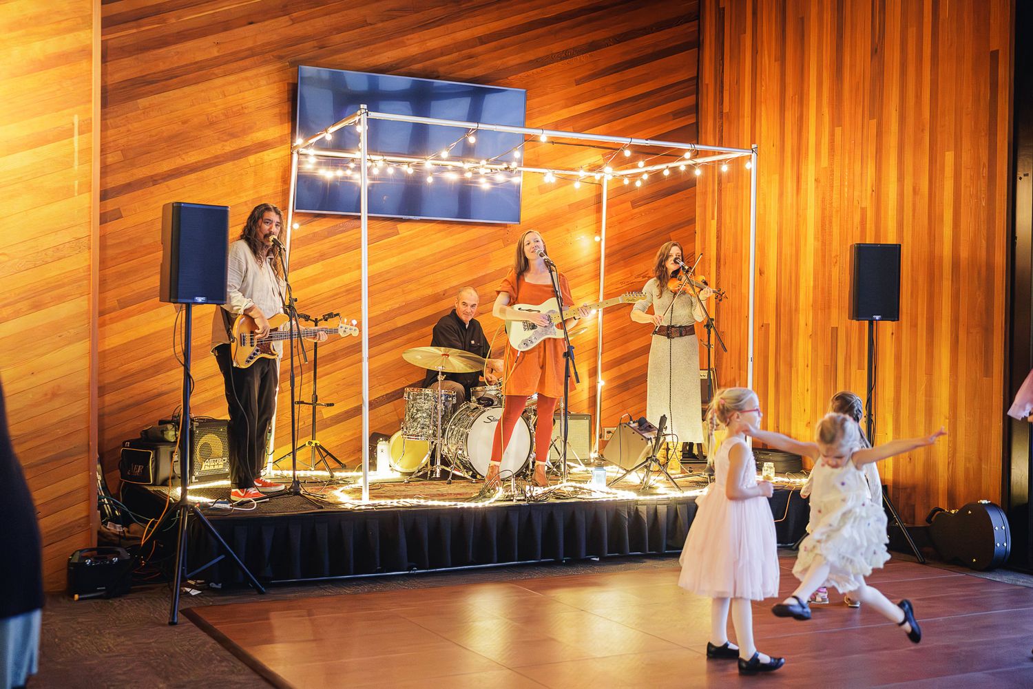 A live band performs on stage while young children in white dresses dance at a wedding reception.