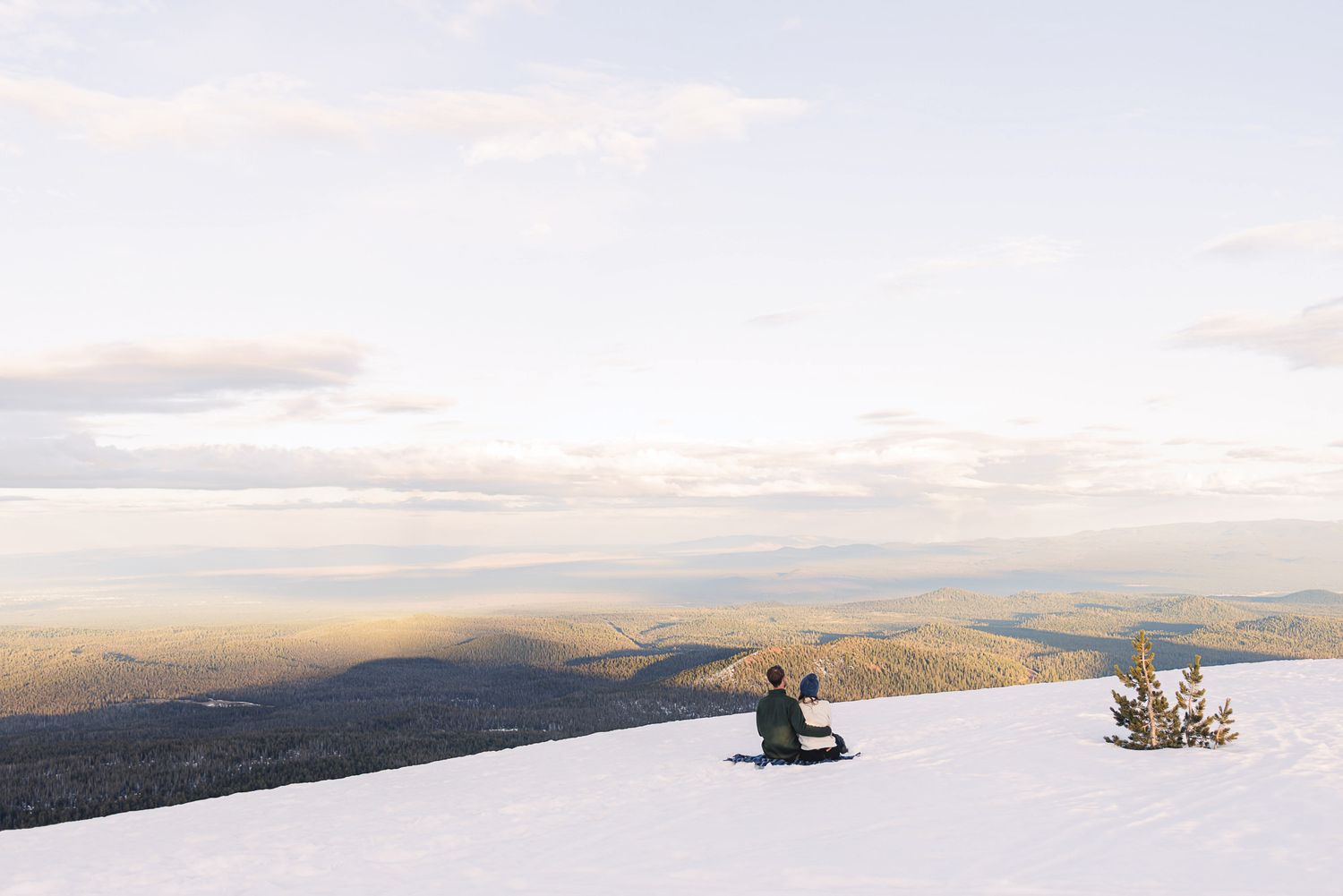 Person sitting on a snowy mountain summit enjoying a breathtaking panoramic winter landscape view at golden hour.