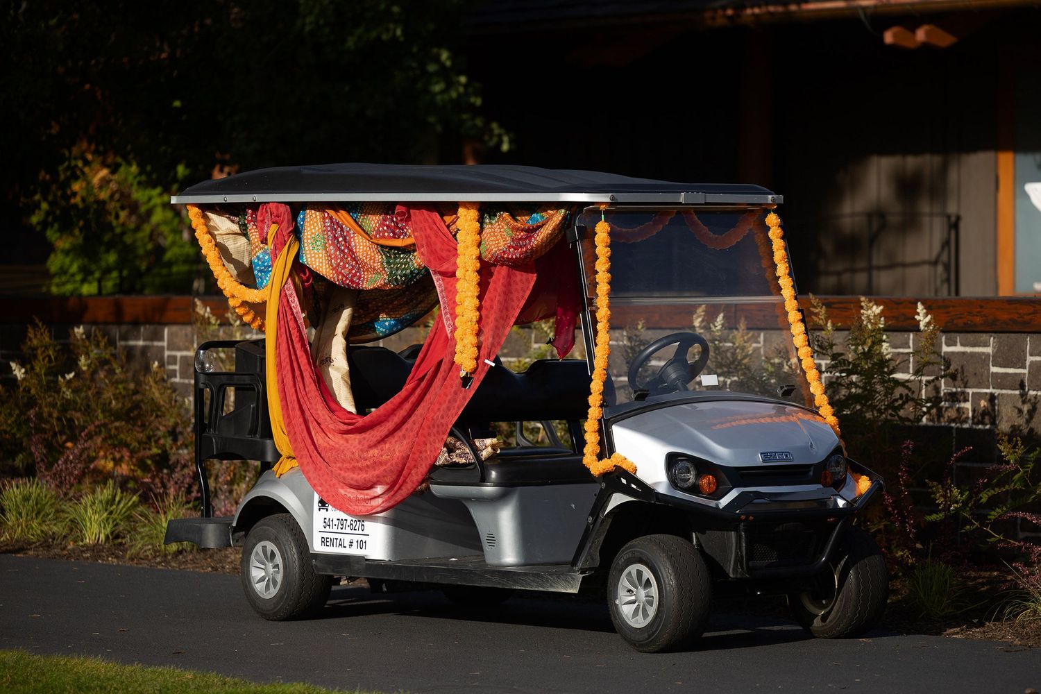 Decorated golf cart adorned with colorful garlands and red fabric draping, parked outdoors near greenery.