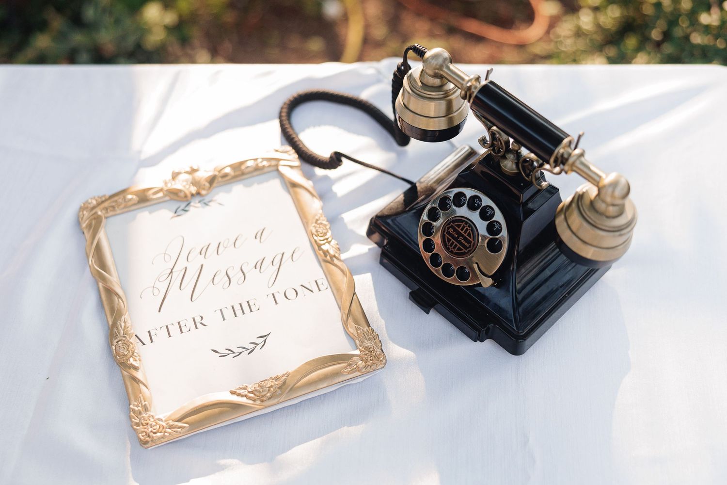 Vintage rotary phone beside a gold-framed wedding guest book sign on a white tablecloth.