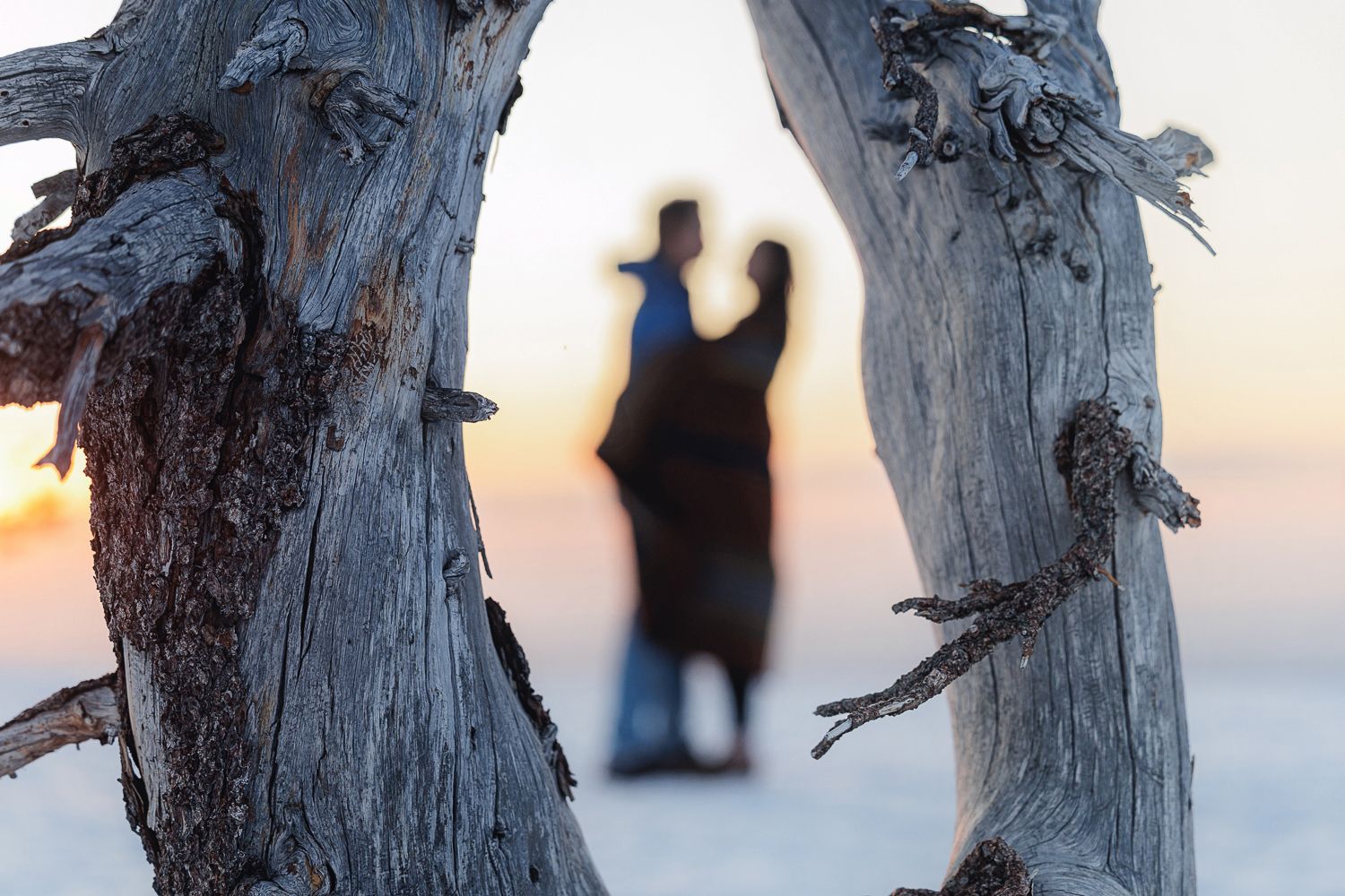 Skiers standing on snowy ground at dusk with a warm sunset glow illuminating a dramatic mountainous backdrop.