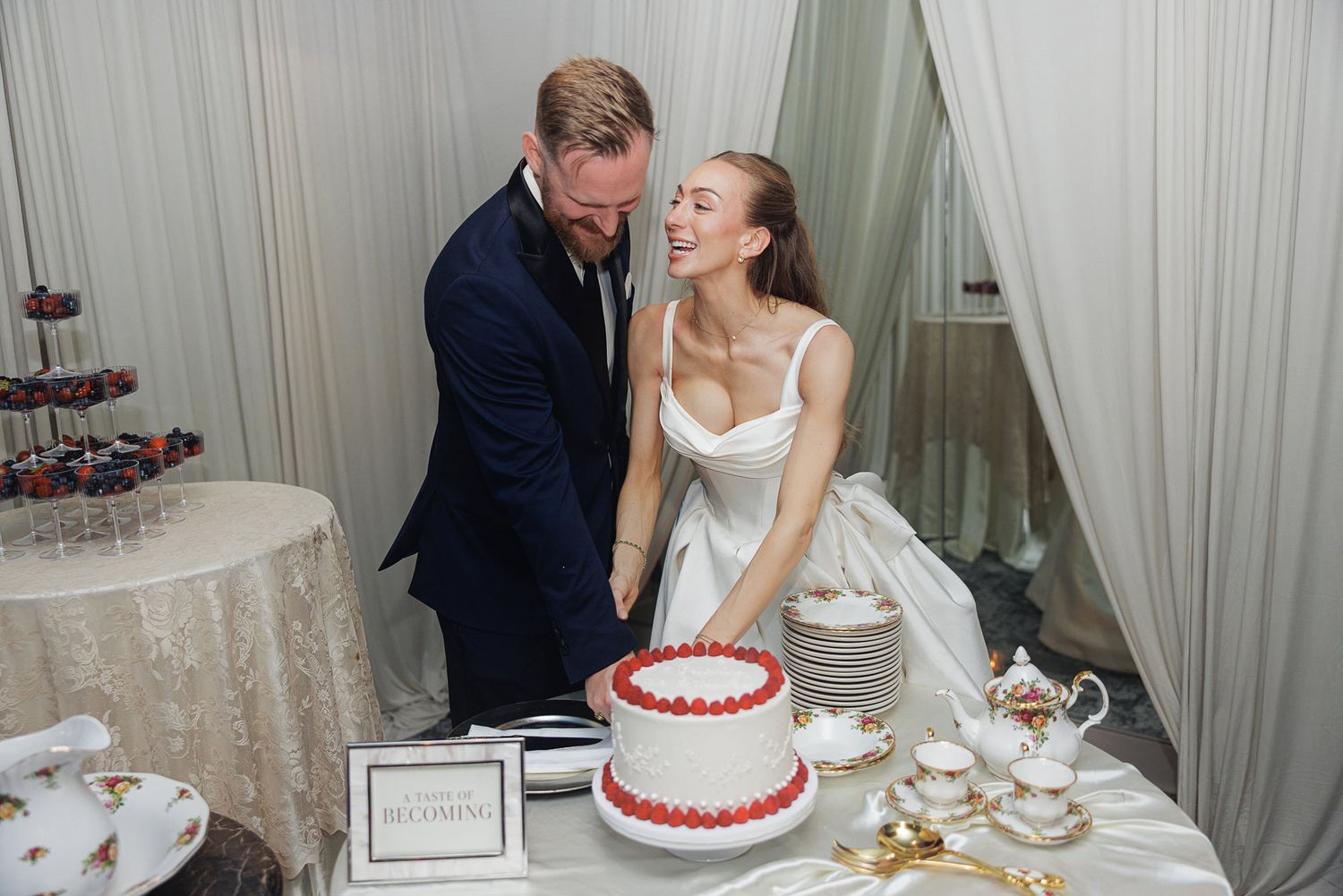 Smiling couple cutting their red and white wedding cake at elegant reception table.