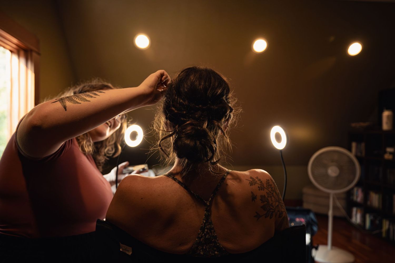 Hair stylist working on an intricate braided updo hairstyle in a dimly lit salon with warm lighting.