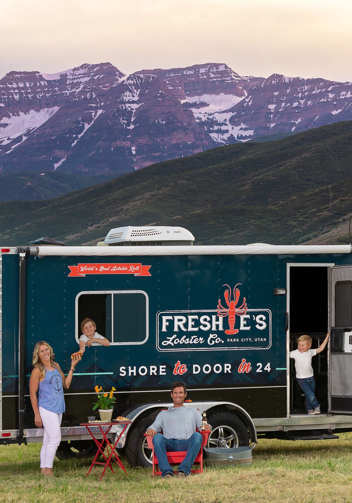 Food truck parked in front of dramatic mountain landscape at sunset.