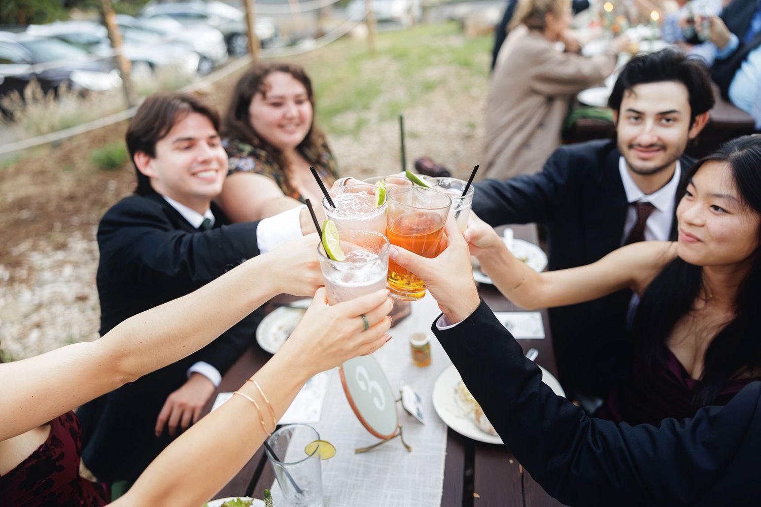 A diverse group of friends toasting with cocktails at an outdoor wedding reception celebration.