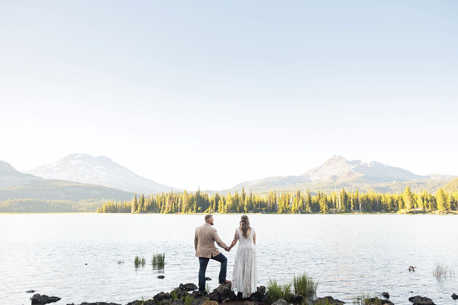 A couple shares a romantic moment on a wooden dock overlooking a serene mountain lake at sunset.