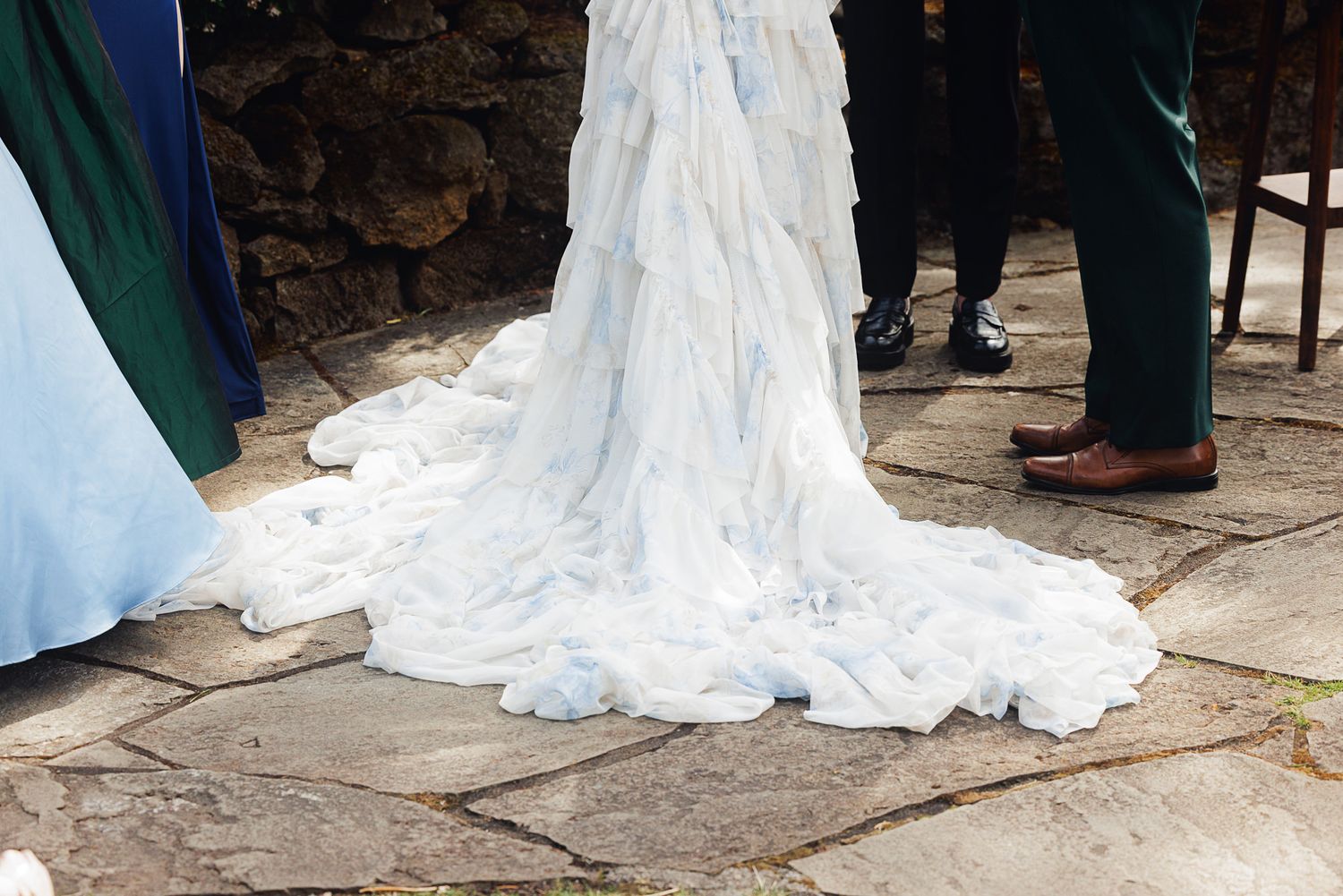 A bride wearing a flowing white and light blue wedding gown with a long train on a stone patio.