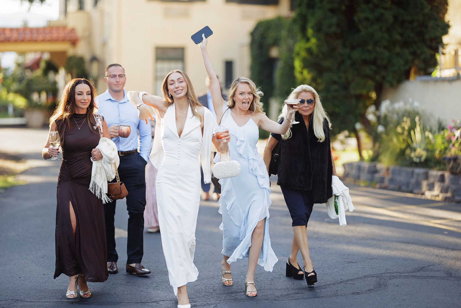 Group of elegantly dressed women walking outdoors, celebrating at a wedding venue on a sunny day.