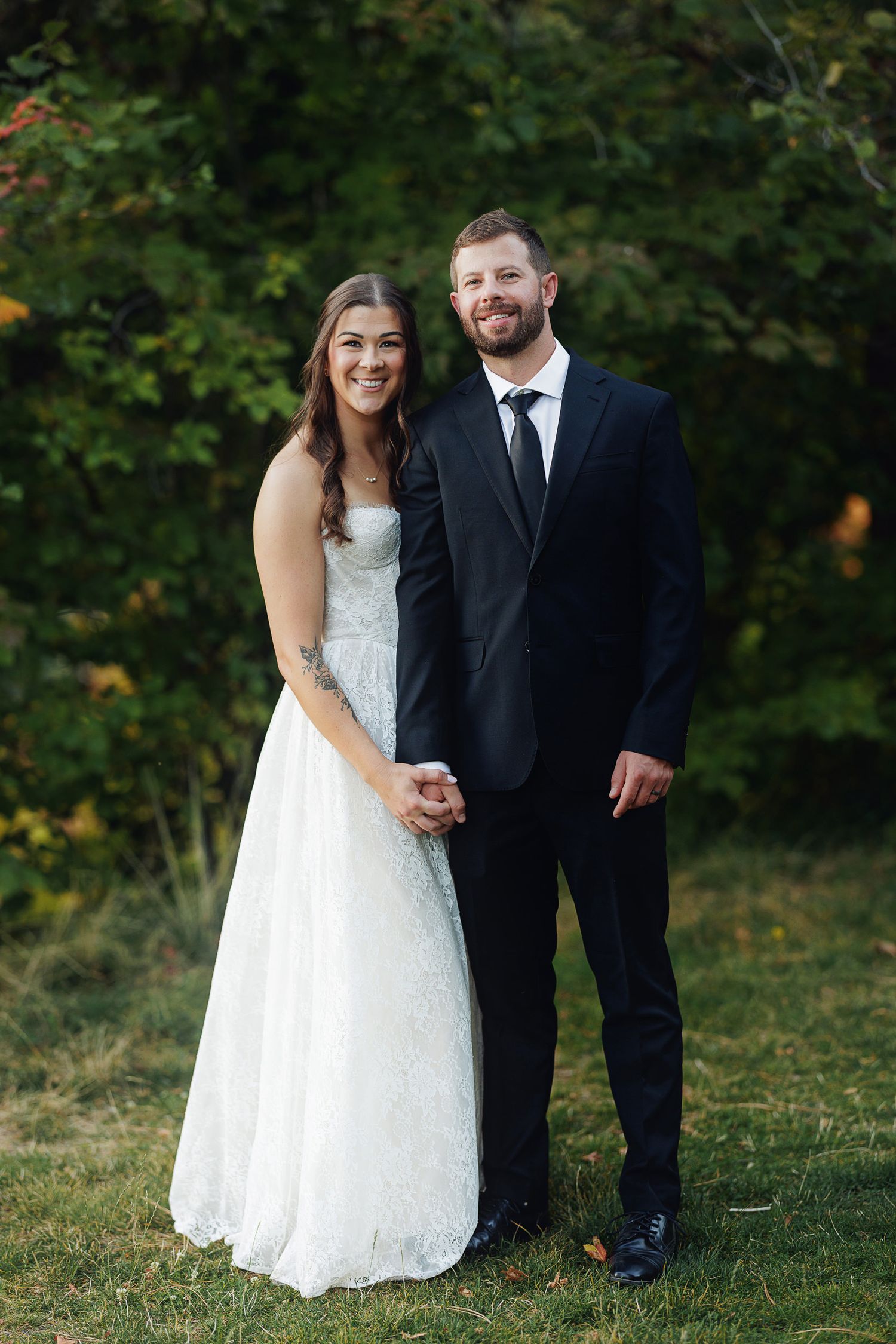 Bride in white gown and groom in black suit hold hands outdoors on their wedding day.
