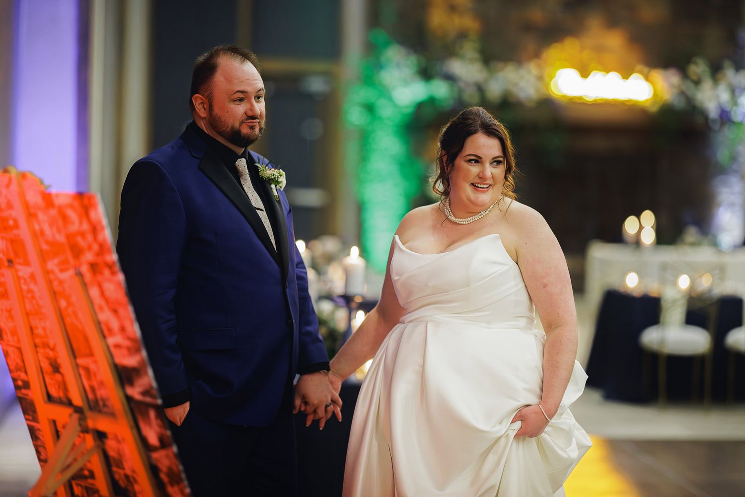 A couple in formal wedding attire stands together during their reception celebration.