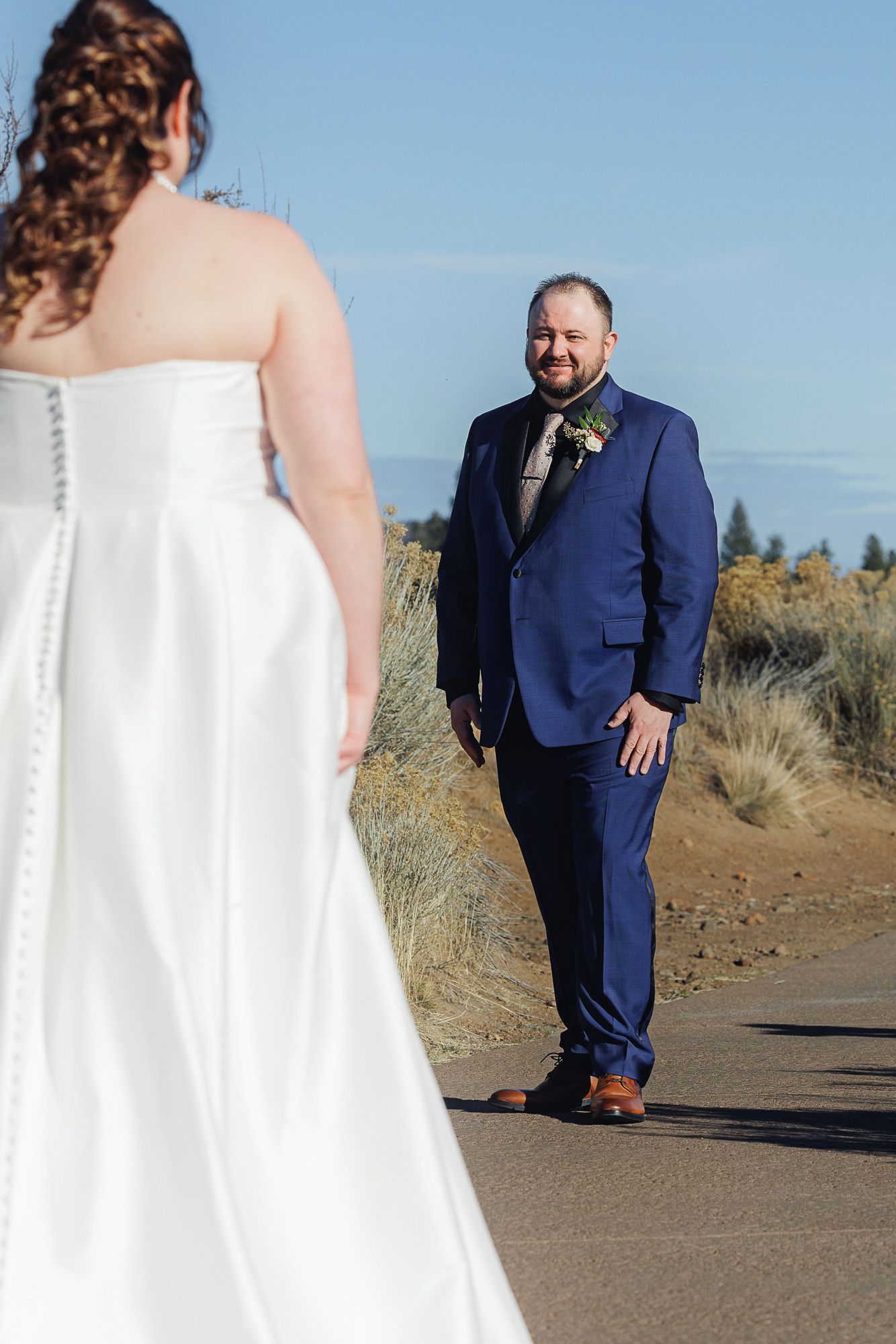 A couple shares a first look moment on their wedding day, with the bride in white and groom in navy on a desert path.
