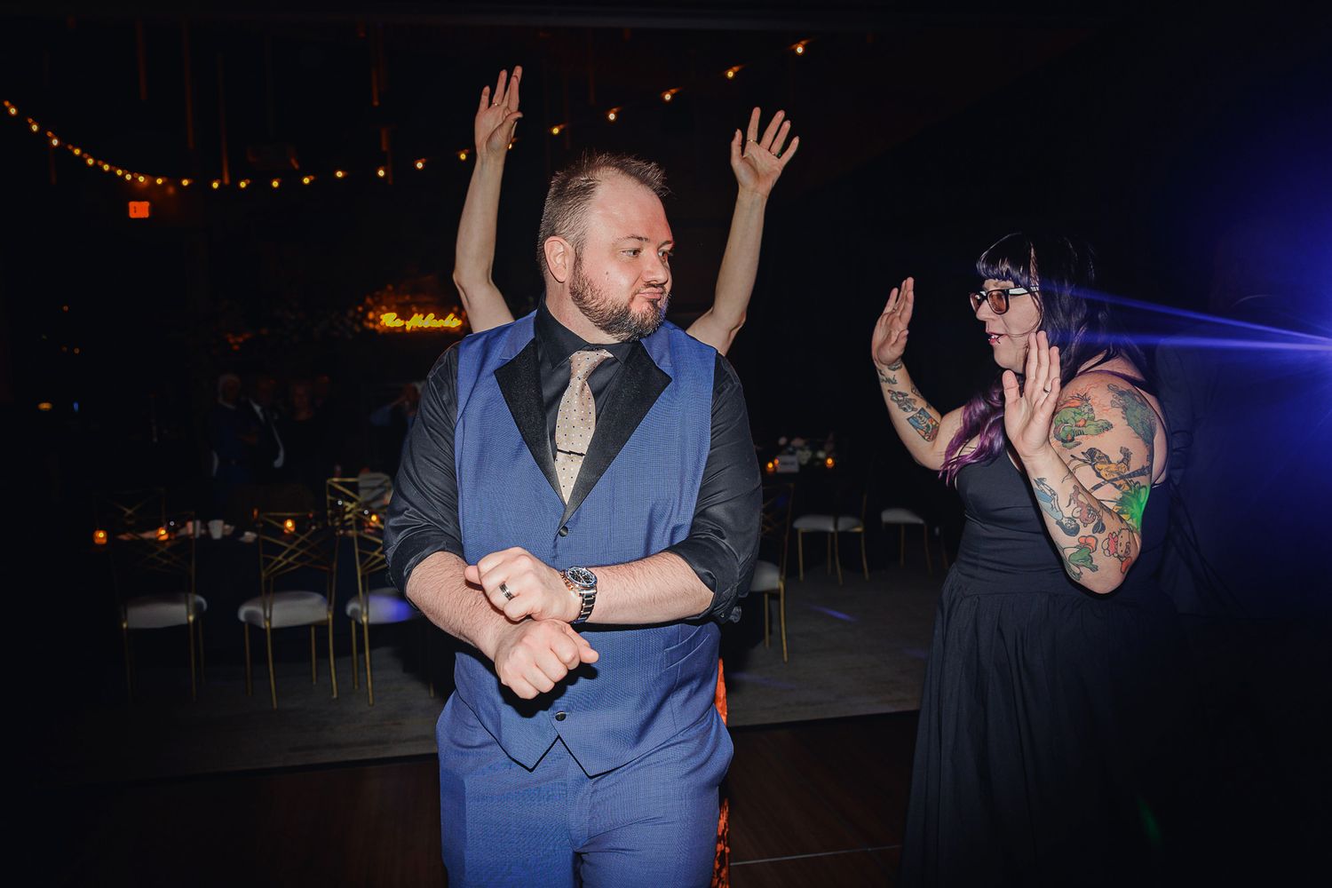 People dancing and celebrating at a nighttime outdoor event with string lights overhead.