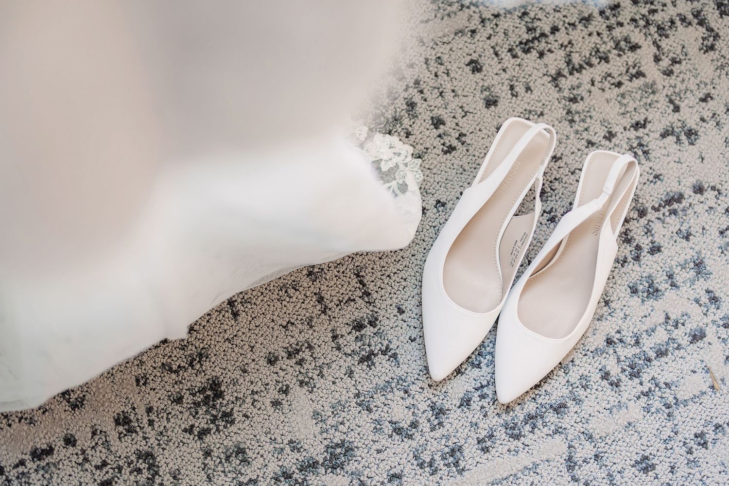 White pointed-toe flats rest on a gray and white patterned area rug with geometric designs.